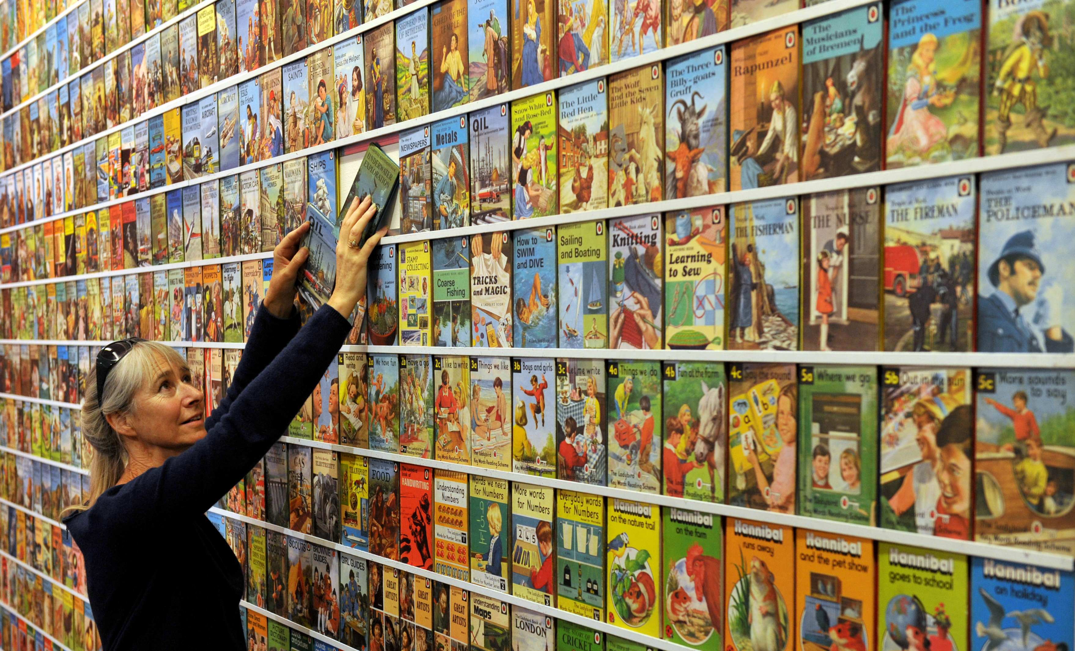 Image: Helen Day, Ladybird expert and enthusiast, standing beside a wall of colourful Ladybird books