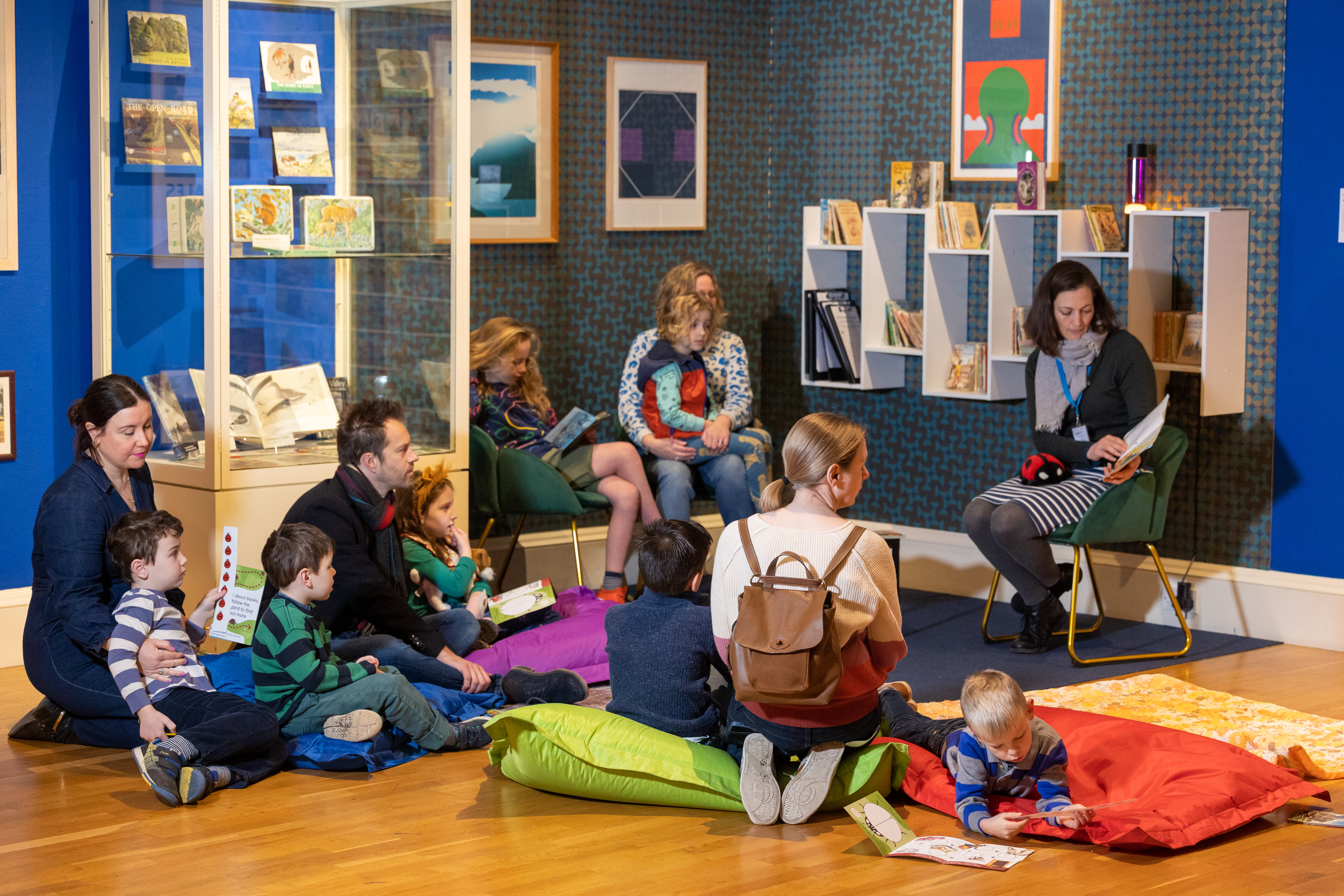 Children sit around a storyteller in a dark blue gallery room