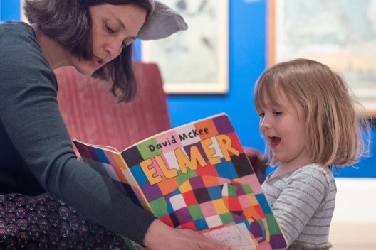 a woman reading  Elmer the Elephant book to a young girl in an art gallery