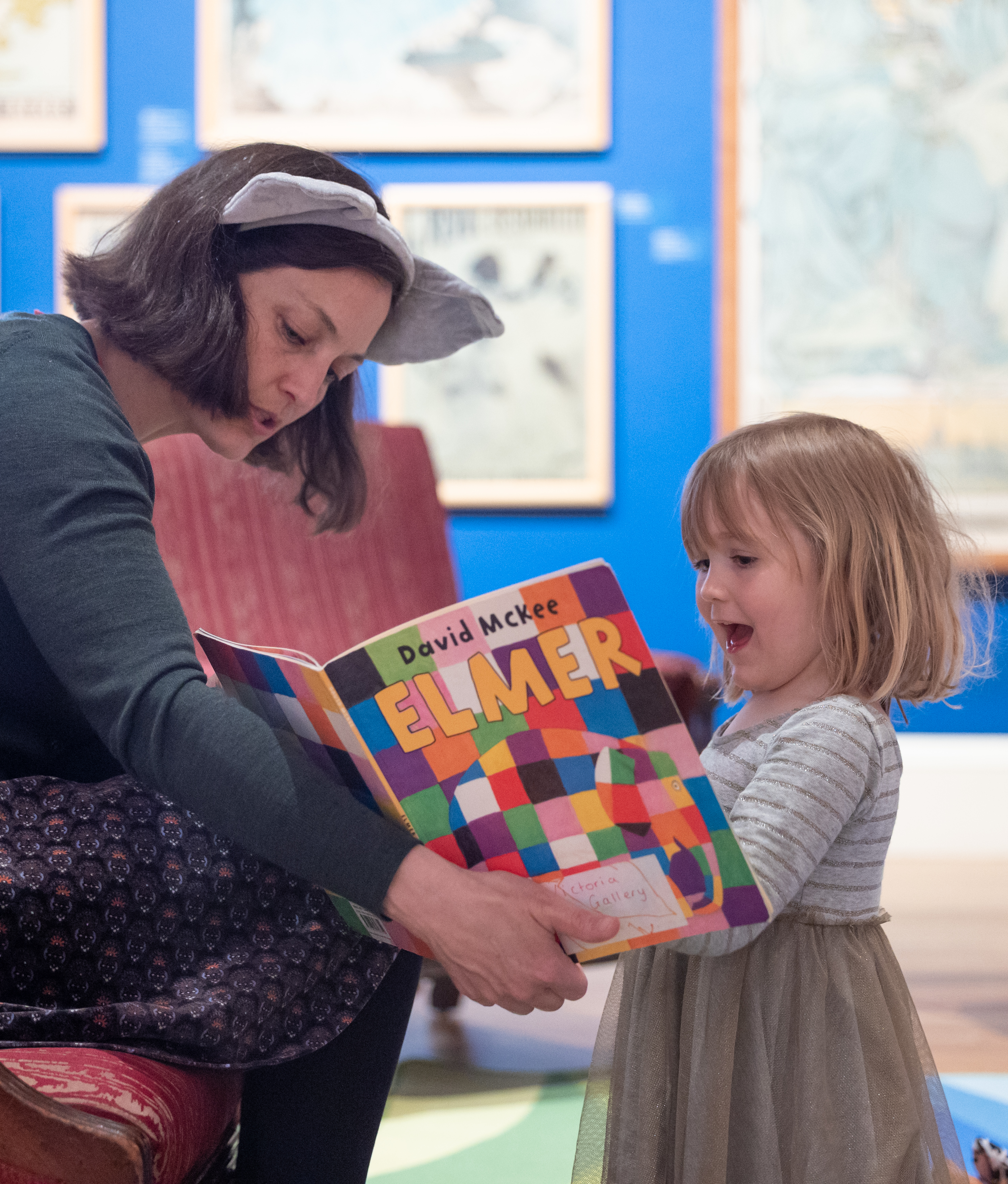 a woman reading Elmer the Elephant book to a young girl in an art gallery